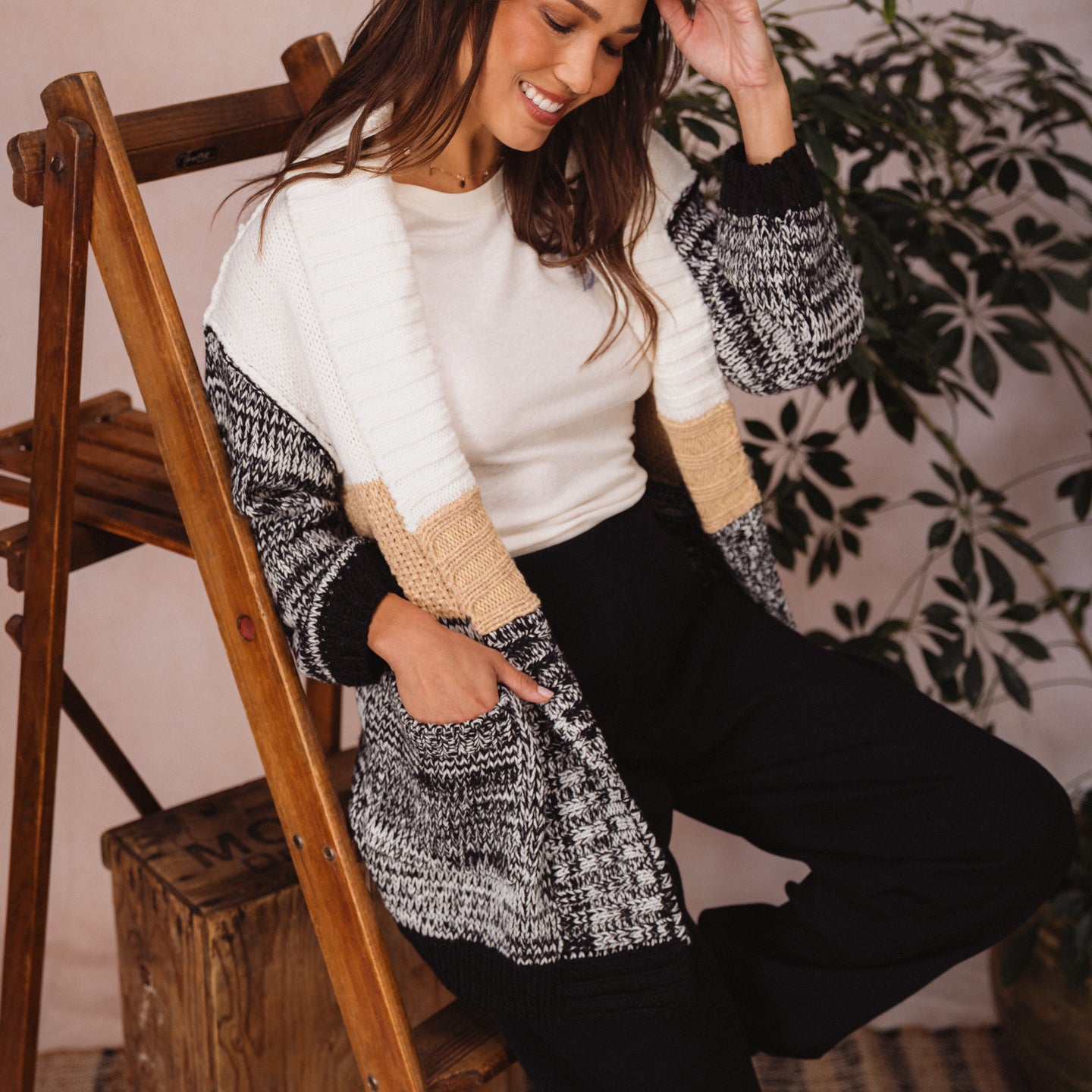 Woman wearing the oversized Hazy Sweater Cardigan with chunky yarns, colorblocking, and patch pockets sitting comfortably indoors