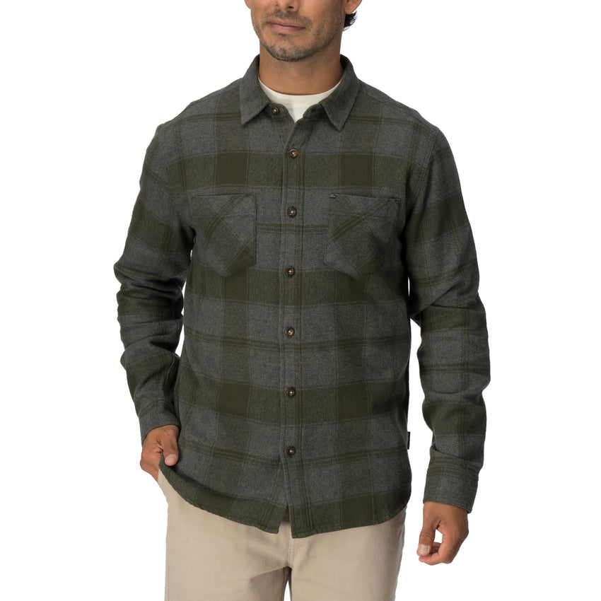 Man wearing a dark green and gray plaid Reggie Flannel Shirt with chest pockets, styled casually for cool weather.