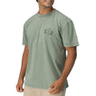 Man wearing a faded green Twining Short Sleeve Tee showing vintage-inspired chest graphic, casual beach apparel.