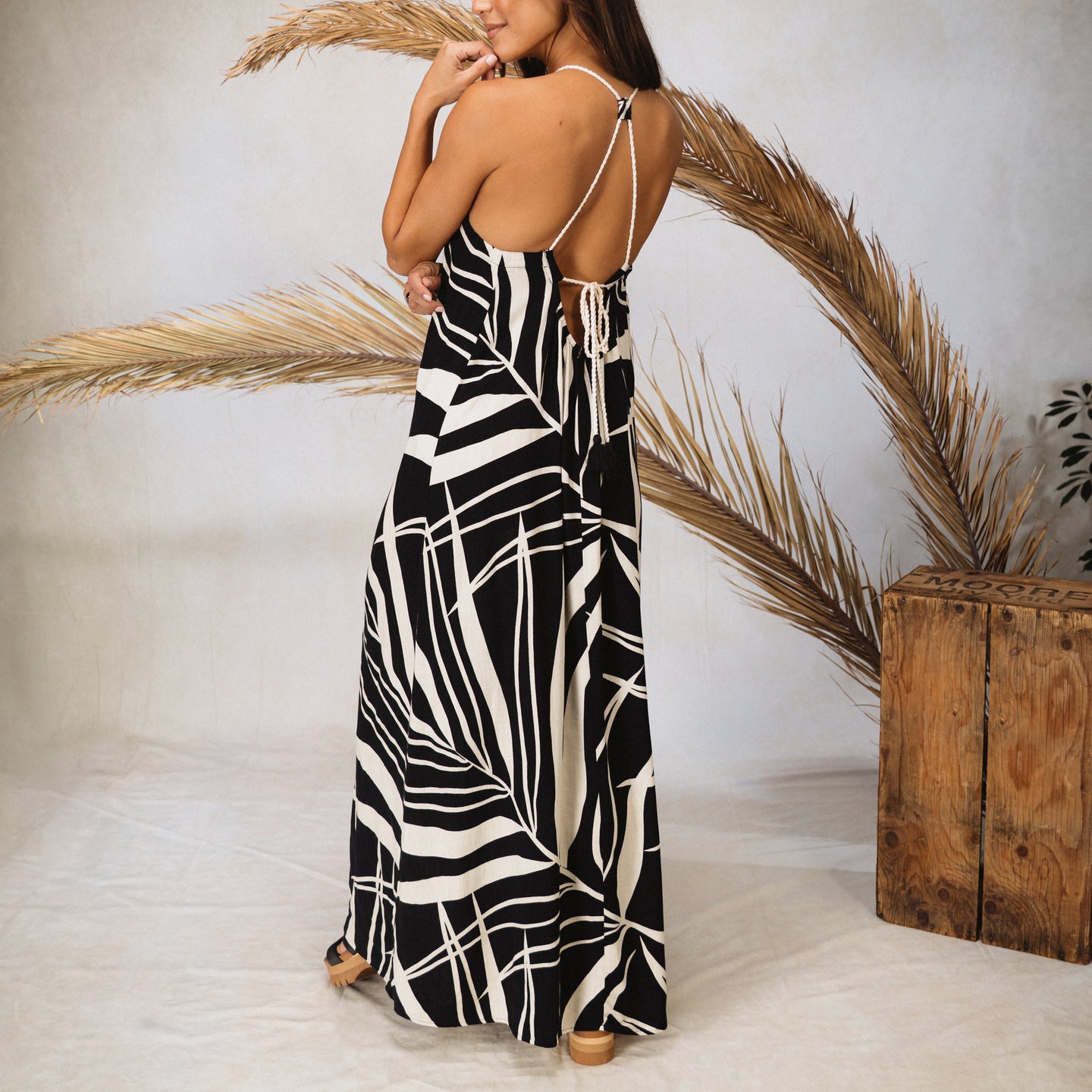 Woman wearing Tori Linen Maxi Dress with black and white print, adjustable halter straps shown from back, relaxed beach style.