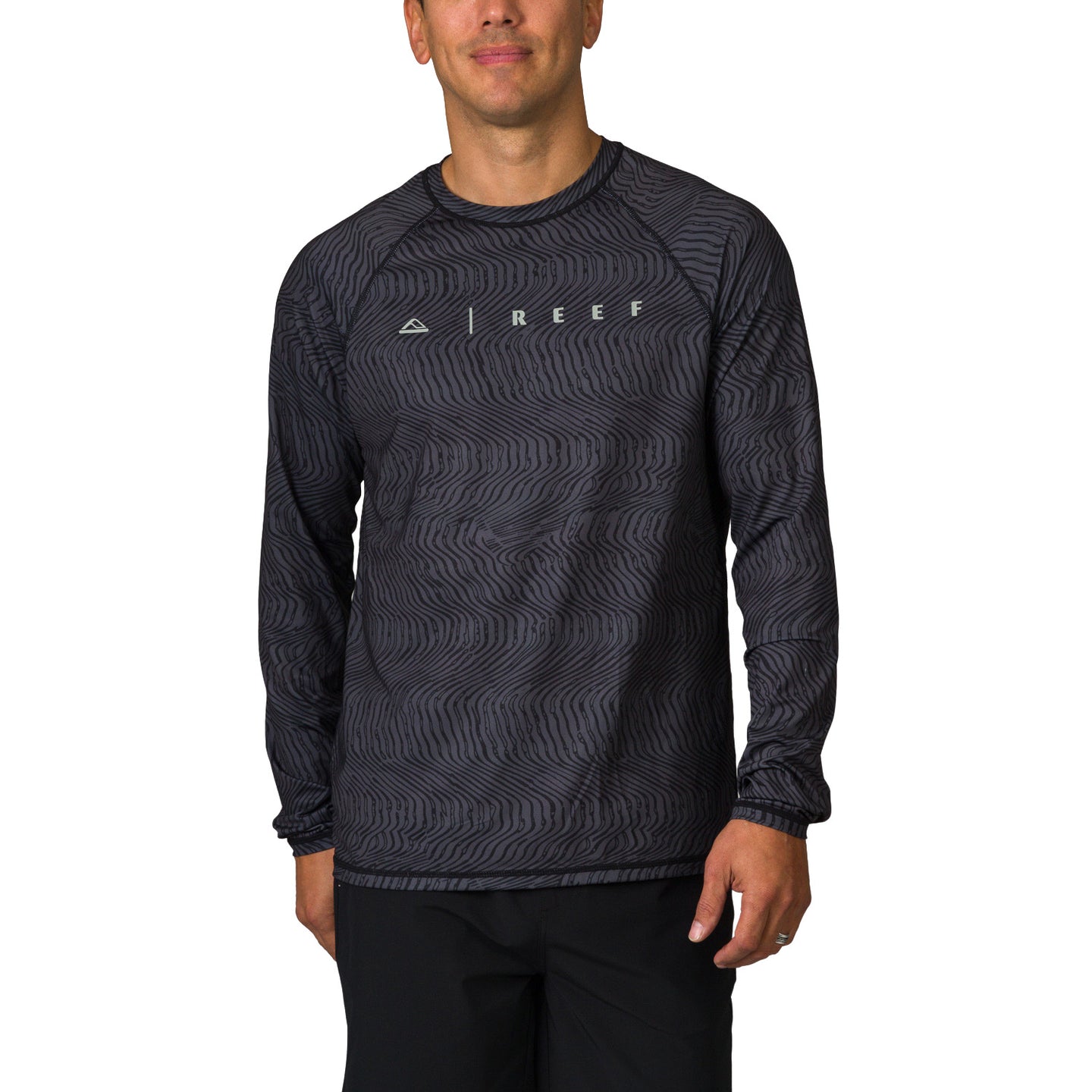 Man wearing a black wave-patterned Dune Performance Shirt facing front, highlighting comfort and surf-inspired design.