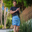 Man wearing blue patterned Fayder Boardshort standing outdoors by plants and wooden fence in casual black shirt