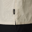 Close-up of the side hem detail on the Harold Camp Shirt showing REEF brand tag on beige, surf-inspired apparel.