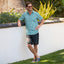 Man wearing Hartman Woven Shirt in teal print, standing outdoors with relaxed pose, wearing navy sandals facing forward