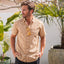 Man wearing the Hartman Woven Shirt in beige with tropical pattern, hands in pockets, standing by palm plants outdoors