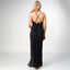 Woman wearing black Plisse Dress facing away, showing back detail with thin crossed straps and tie closure, standing in sandals.