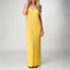 Woman wearing a yellow Plisse Dress with spaghetti straps, standing and smiling, showcasing flowy beach-inspired apparel.