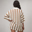 Woman wearing Mika Button Down Top in white with brown stripes, shown from back, featuring relaxed fit and textured knit fabric.