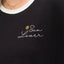 Close-up of the chest area on the Sun Lover Ringer Tee showing black fabric, white collar, and embroidered sun and text design.