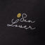Close-up of embroidered "Sun Lover" text with yellow sun detail on black fabric of the Sun Lover Ringer Tee for women.