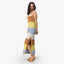 Woman wearing a striped brown, yellow, blue, and white Gia Maxi Dress with sandals facing left, side view, smiling