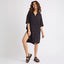 Woman wearing black Ollie Shirt Dress with short sleeves and front buttons, paired with black platform sandals facing right side.