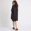 Woman wearing a black Ollie Shirt Dress seen from back, paired with black platform sandals facing right, surf-inspired comfort style.