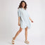 Woman wearing Ollie Striped Shirt Dress with light blue stripes, posing with left foot facing forward in white platform sandals