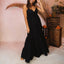 Woman wearing a black Yuni Maxi Dress with a deep notched neckline and tie detail, styled in a beach-inspired setting.