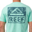 Back view of a man wearing a mint green Wellie Too Tee with a large dark blue REEF logo, casual beach apparel.
