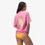 Woman wearing a pink Haus Boyfriend Crew shirt facing backward, showcasing the back design in a relaxed beach style.
