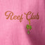 Close-up of pink Haus Boyfriend Crew fabric showing "Reef Club" text and embroidered palm tree charm, surf-inspired comfort.