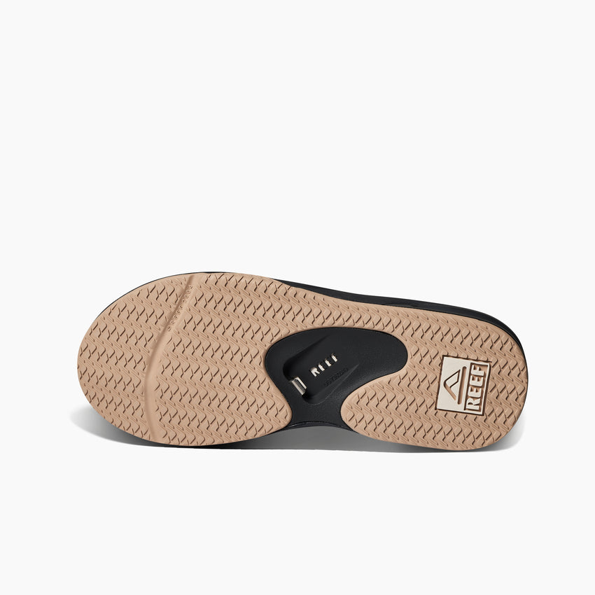 Fanning men's shoe sole facing up showing tread pattern and anatomical arch support with REEF logo for comfort.