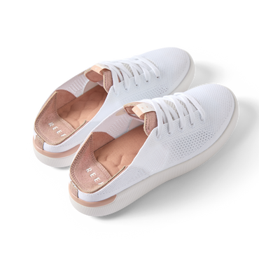Reef Neptune women's white and rose gold sneakers angled side view showing lightweight knit upper and cushioned heel.