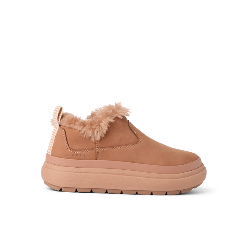 Side view of a tan slip-on shoe facing right with plush lining and thick cushioned sole for beach comfort.