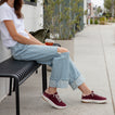 Reef Del Mar burgundy sneakers facing right on a woman seated outdoors