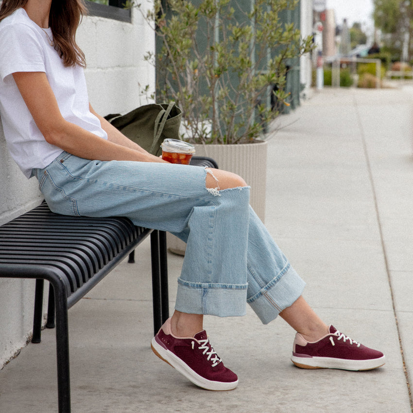 Reef Del Mar burgundy sneakers facing right on a woman seated outdoors