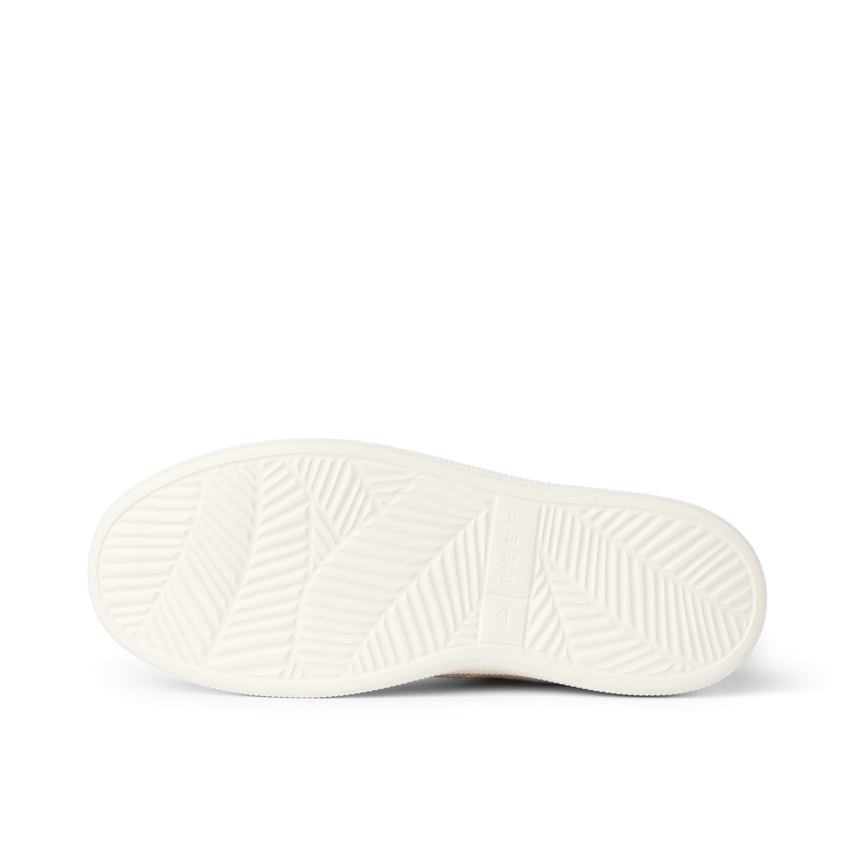 White footwear sole viewed from below, facing left, with textured traction grooves and a cushioned footbed pattern