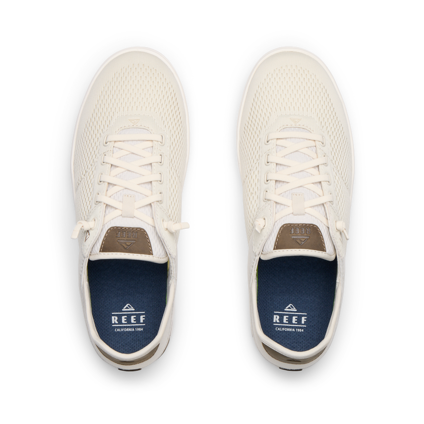 Top view of pair of cream-colored REEF sneakers facing upward with mesh uppers and blue cushioned insoles.