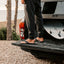 Cushion Phantom 2.0 sandals facing right on adult male feet, shown from side near vehicle tailgate and surfboard.