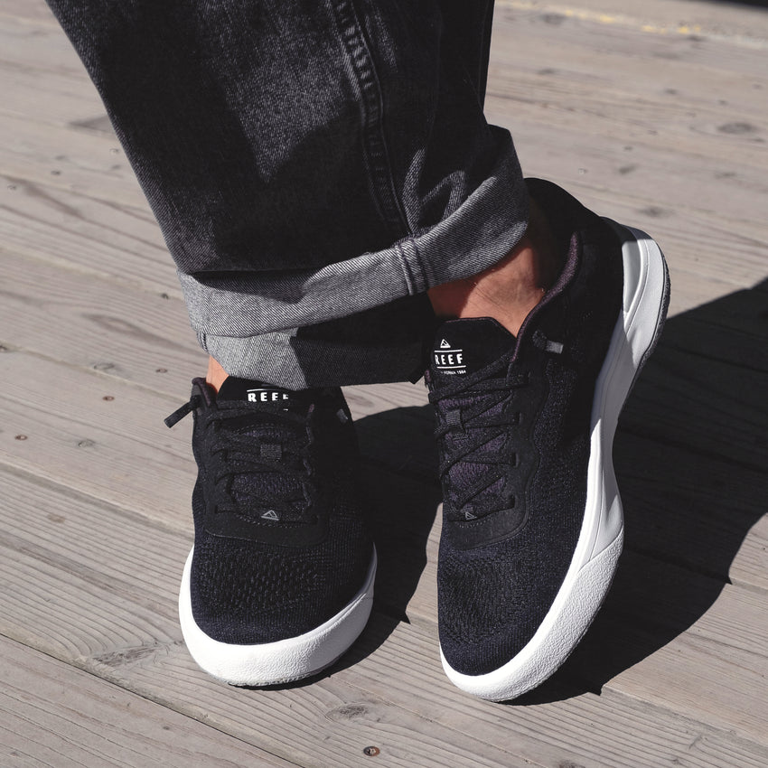 Pair of Shoreline Del Mar sneakers facing forward on wooden deck, highlighting black sustainable design and cushioned comfort.