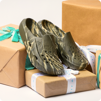 Pair of camouflage clogs facing forward with perforated uppers and molded footbeds on wrapped boxes