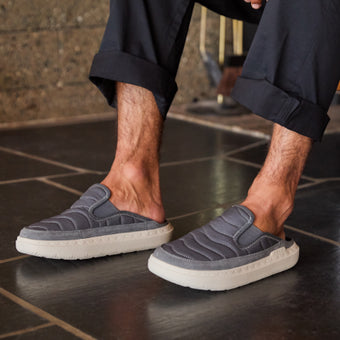 Gray cushioned slip on shoes facing left on a tiled floor