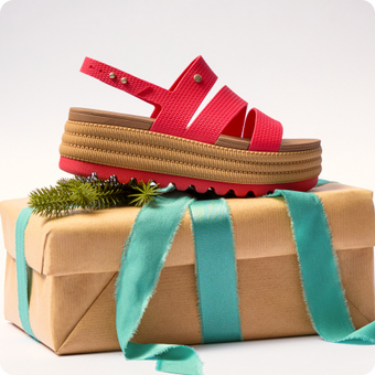 Red platform sandal facing right atop a wrapped gift with greenery and teal ribbon