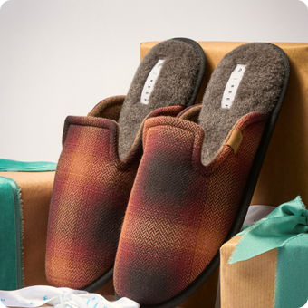 Pair of burgundy and brown closed toe slip on shoes facing forward on gift boxes