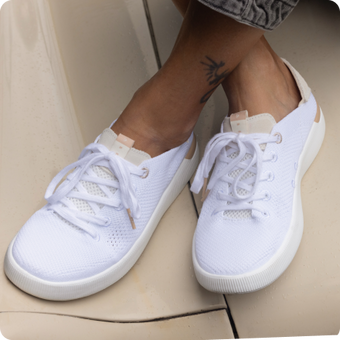 White sneakers facing toward the viewer, with mesh uppers, laces, and cushioned soles