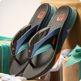 Pair of REEF blue and black flip flops facing toward the lower left with textured footbeds and cushioned soles