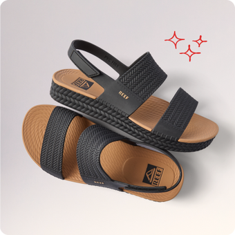 Two black REEF sandals facing opposite directions, with woven straps and tan cushioned footbeds