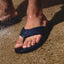 Fanning H2O sandal facing forward on wet foot with water droplets, navy blue water-friendly flip flop with cushioned footbed.