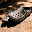 Glider water-friendly clogs facing left, showing perforated uppers and cushioned molded footbeds on a rock surface