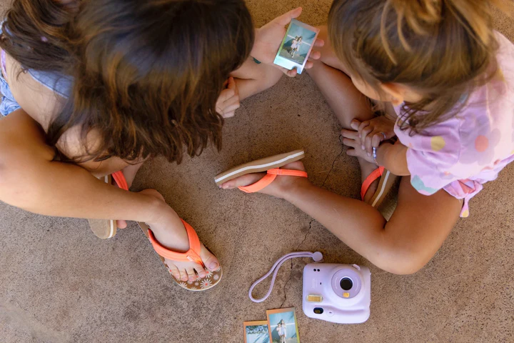 Two girls playing with a polaroid camera looking at photos.