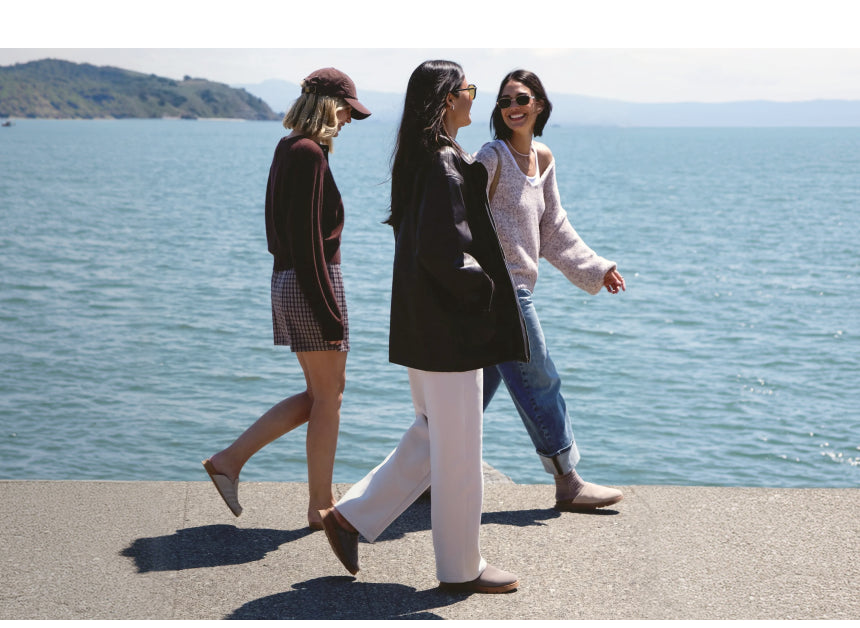 Three women walking along a waterfront wearing casual beach-inspired apparel and comfortable slip-on shoes facing right.