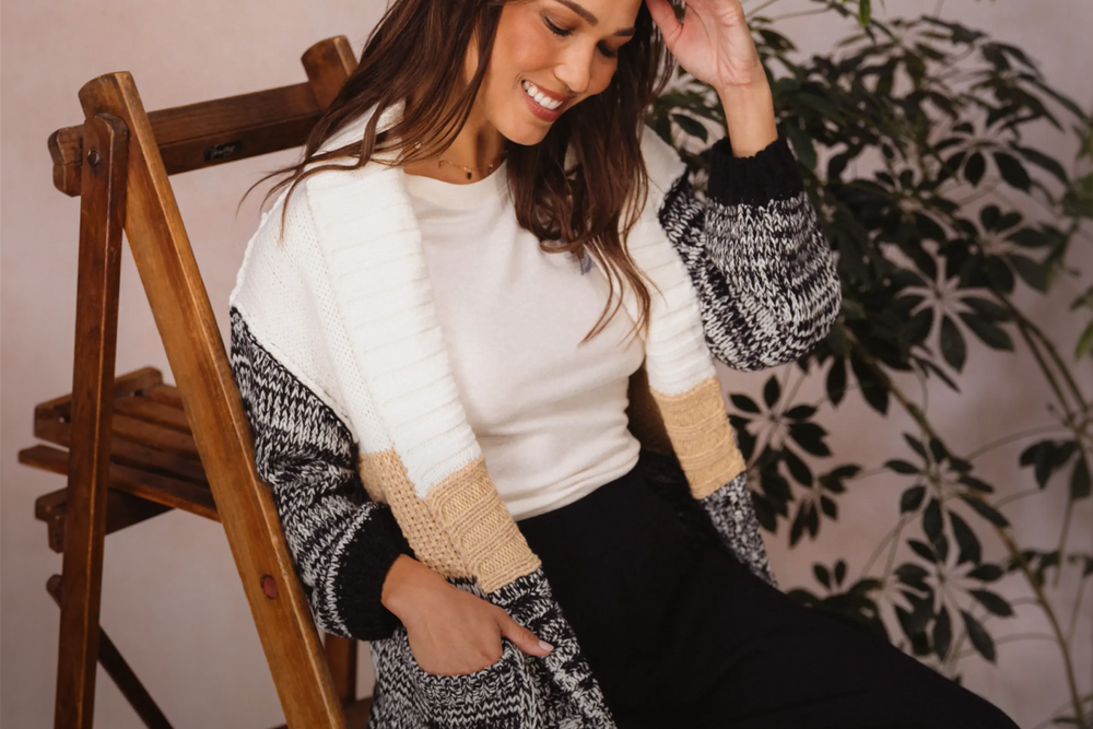 Woman seated on a wooden ladder chair wearing a cozy black, white, and tan knit cardigan