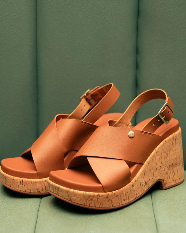 A pair of brown leather and cork wedge heels with a backstrap on a green background