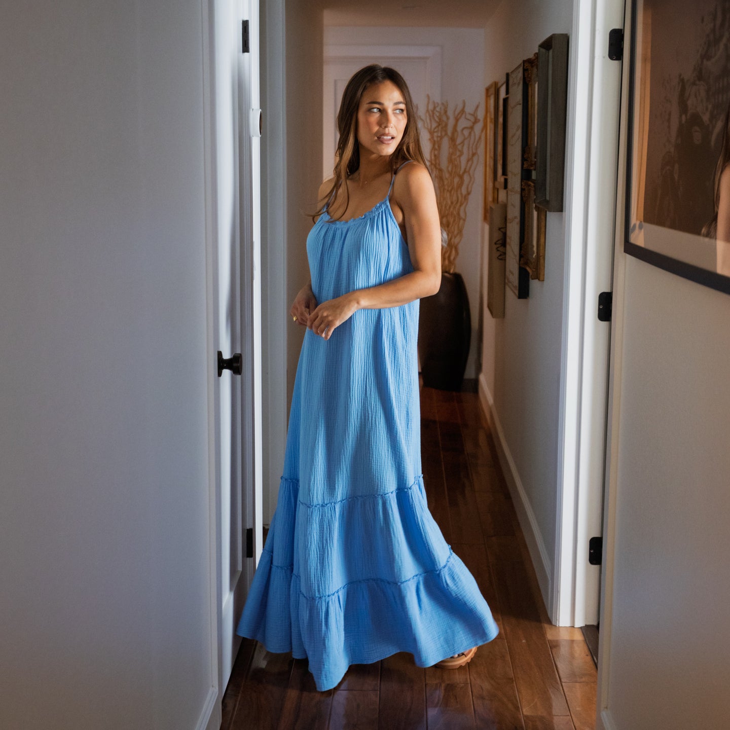 Woman wearing a light blue Lainey Maxi Dress standing in a hallway, showcasing its flowing beach-inspired design.