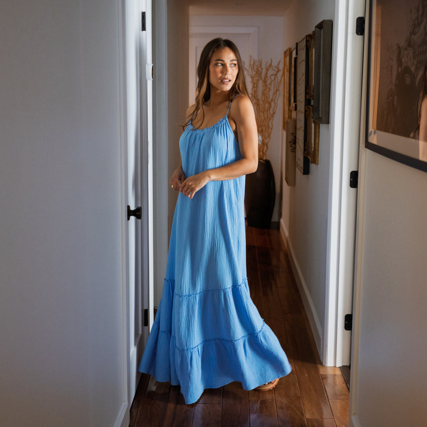Woman wearing a light blue Lainey Maxi Dress standing in a hallway, showcasing its flowing beach-inspired design.