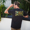 Man wearing black Isac Tee showing back graphic design outdoors, beach-inspired comfort apparel for men.