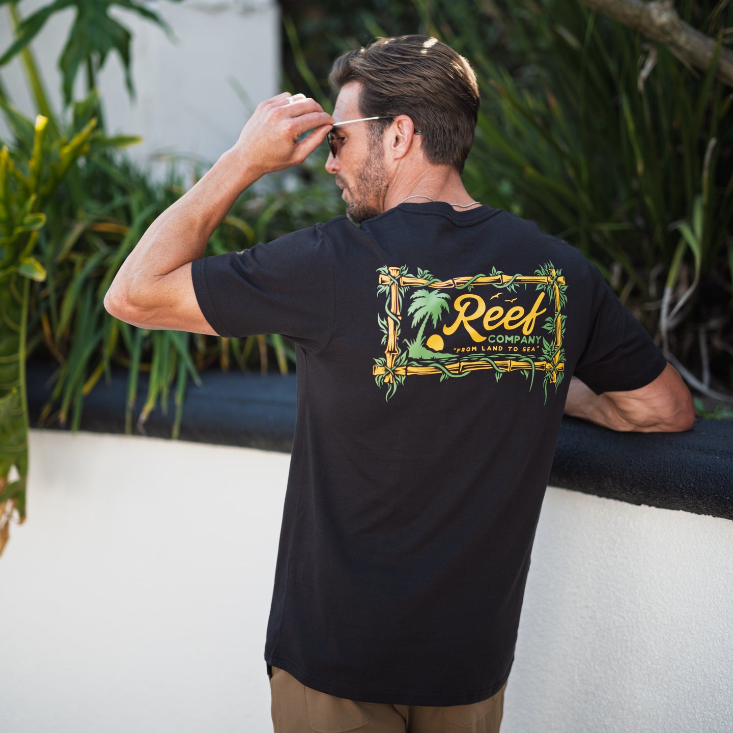 Man wearing black Isac Tee showing back graphic design outdoors, beach-inspired comfort apparel for men.