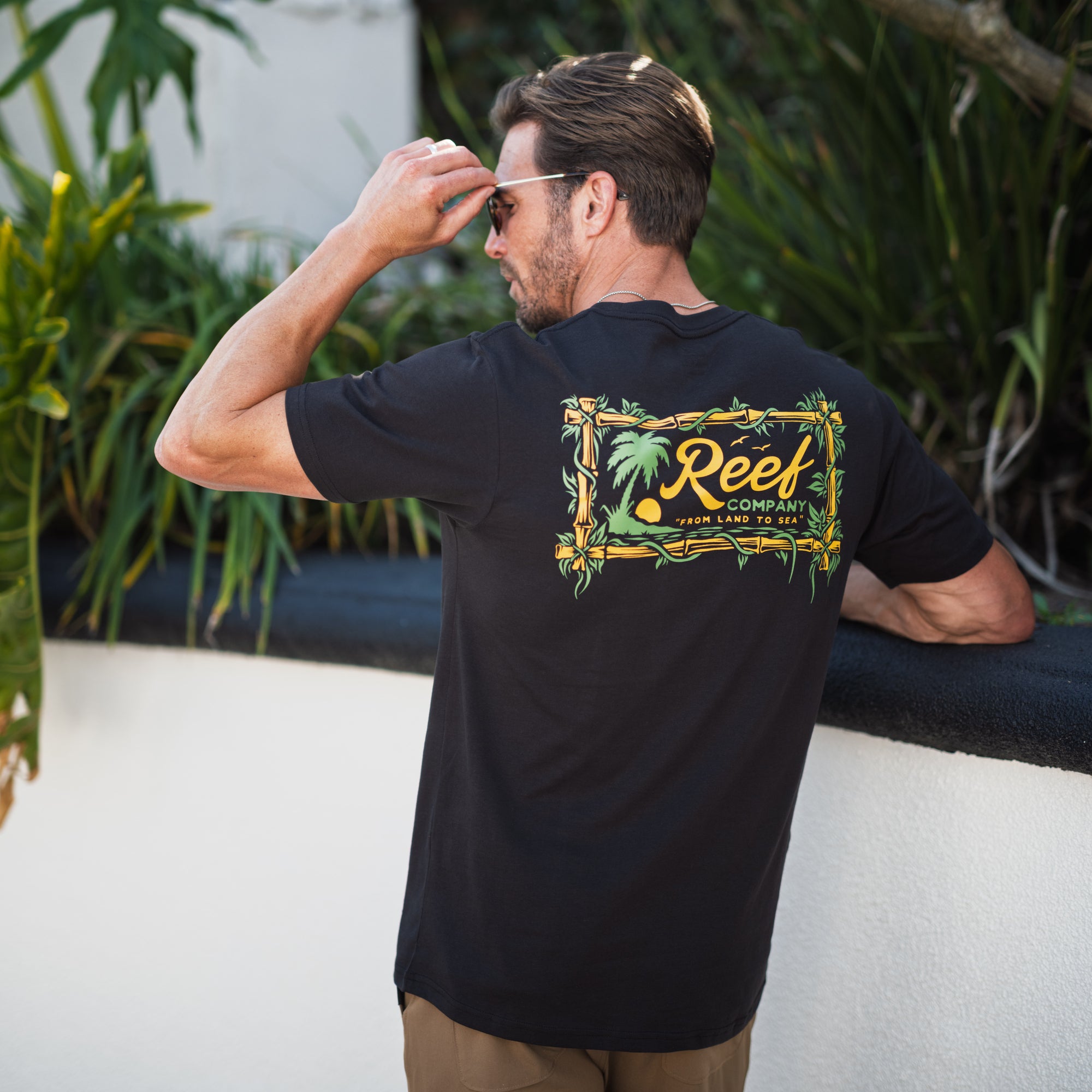 Man wearing black Isac Tee showing back graphic design outdoors, beach-inspired comfort apparel for men.