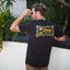 Man wearing black Isac Tee showing back graphic design outdoors, beach-inspired comfort apparel for men.